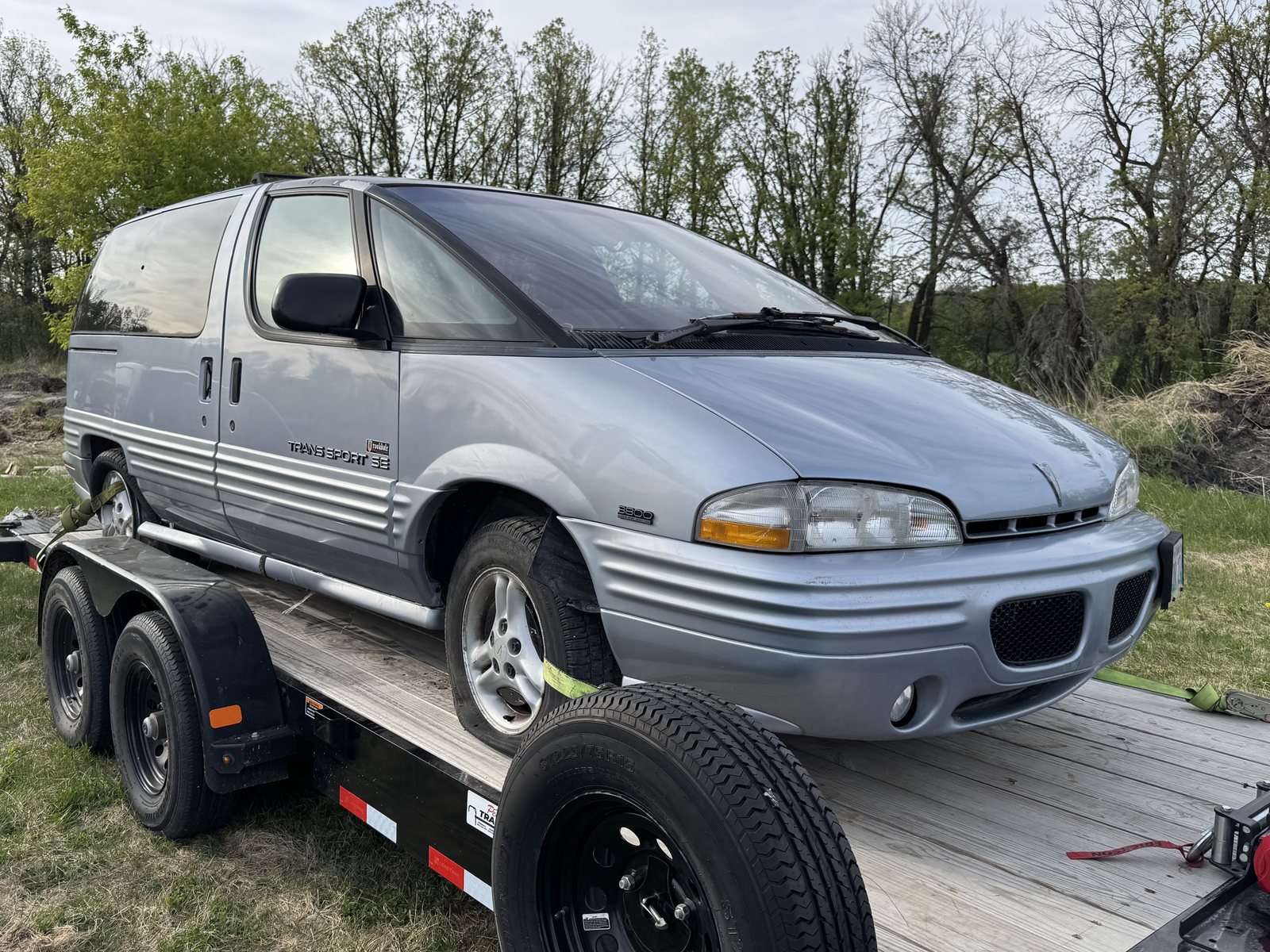 Nineties minivan chained onto a trailer deck at the treeline