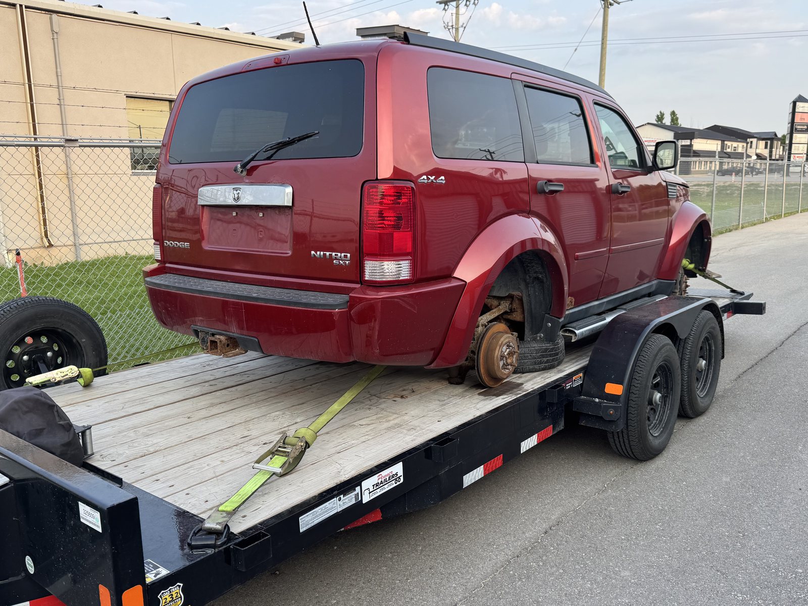 SUV with a missing rear wheel riding on the hub, secured on a flatbed trailer