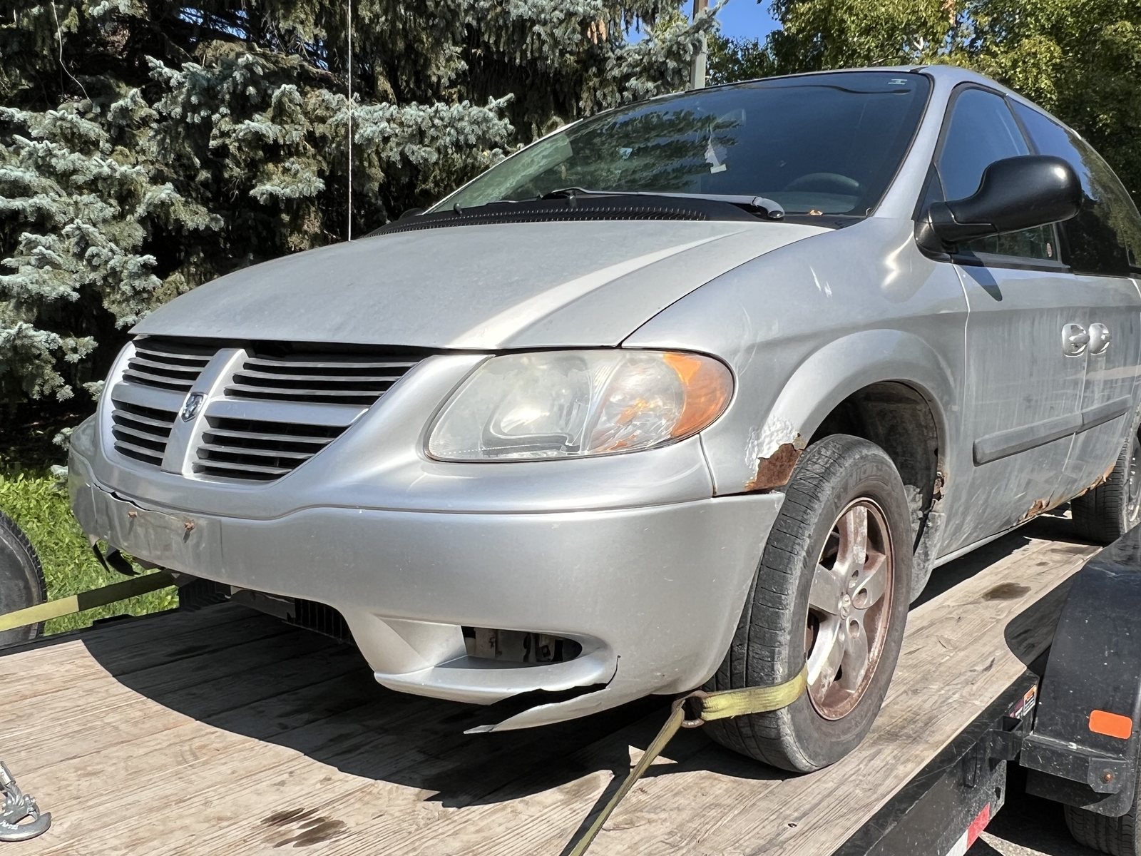 Rusted minivan loaded on a trailer deck, front quarter view